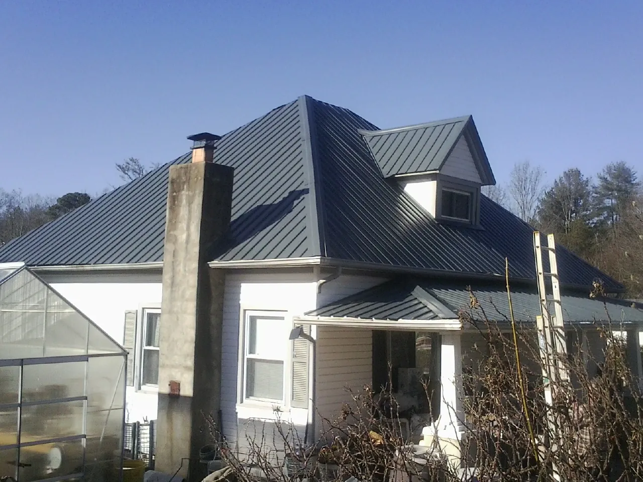 Dark blue standing seam metal roof on a white farmhouse with dormer — Slate & Tile Roof Repair by Roofing Brothers in Leesville