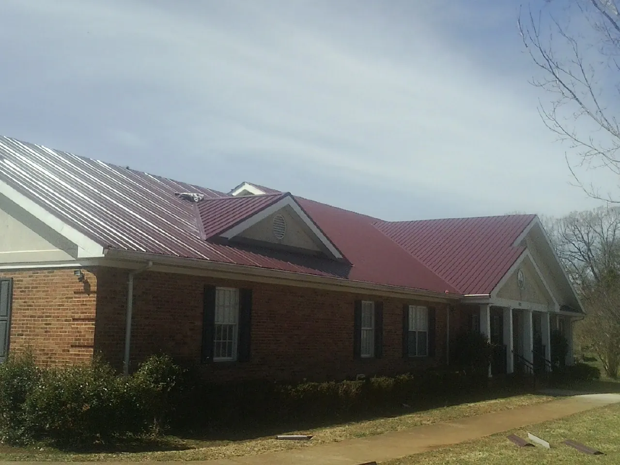 Red metal roof with gabled entries on a long brick building, from a Hail Damage Roof Repair job in Leesville