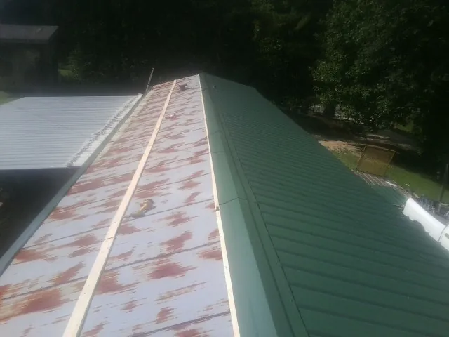 Old rusted panels beside newly installed green metal roofing — Wind Damage Roof Repair by Roofing Brothers in Leesville