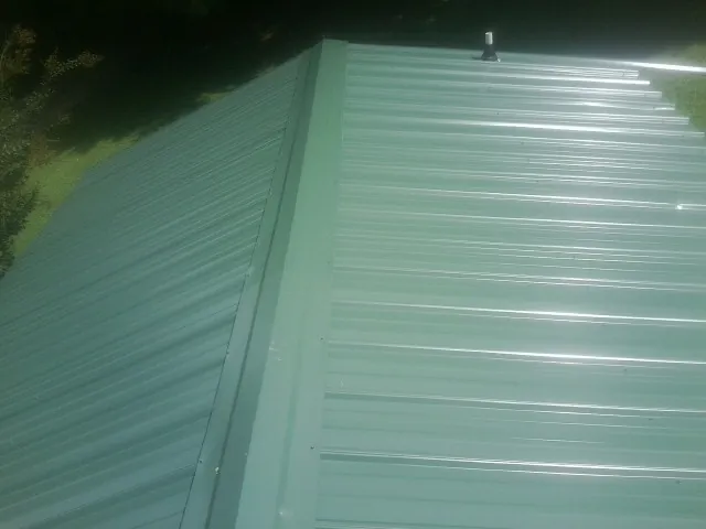 New green metal panels meeting at the ridge of a roof — Flat Roof Repair work by our crew in Leesville