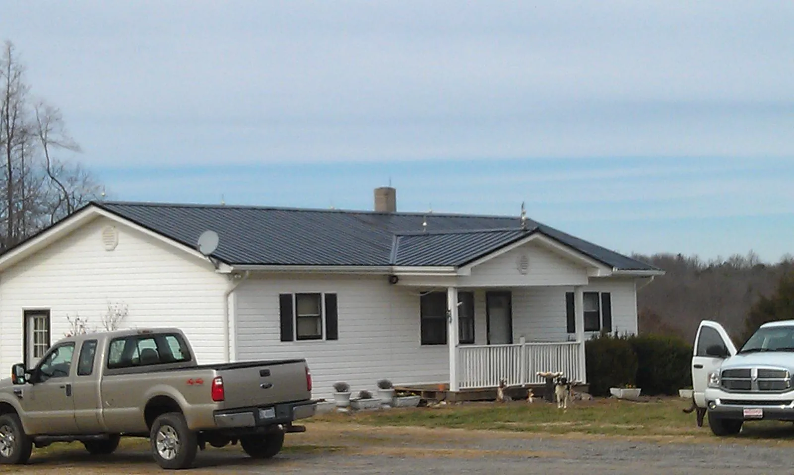 Finished dark metal roof on a white ranch home with work trucks parked in Leesville